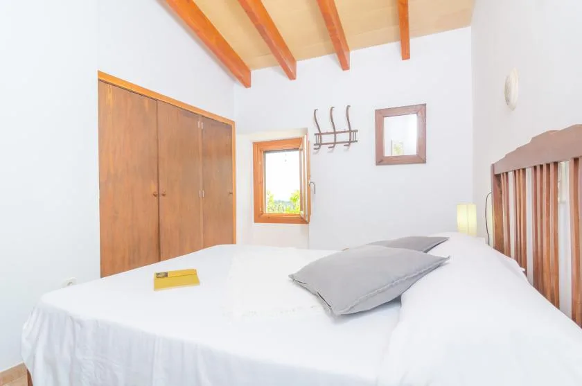 A bedroom with a white bed, wooden wardrobe, and exposed ceiling beams.