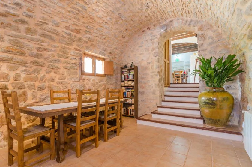 A stone-walled dining area with a wooden table and chairs beside steps.