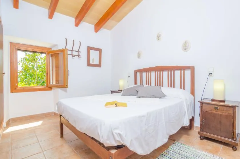A bright bedroom with a wooden bed, white bedding, and an open window.