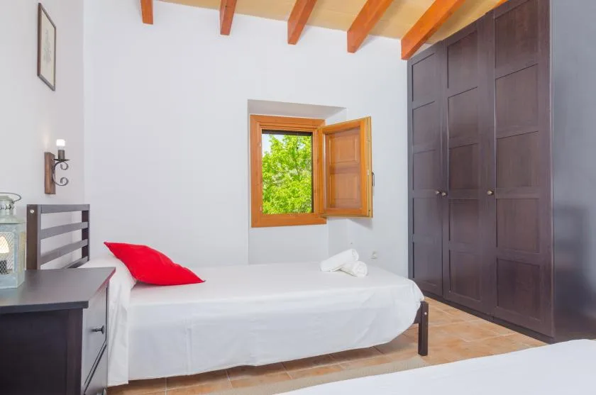 A bedroom with a white bed beside an open window and dark wardrobes.