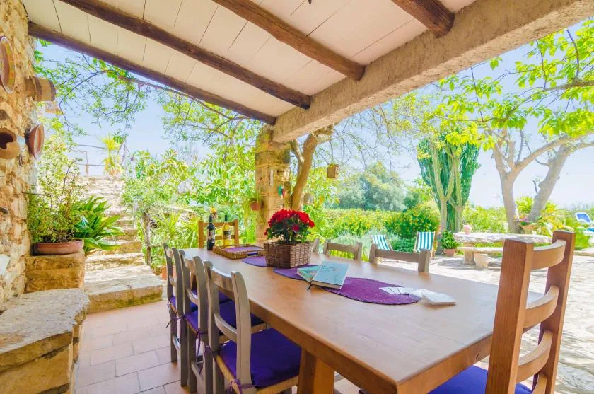 A covered outdoor dining area with a long table overlooking a leafy garden.
