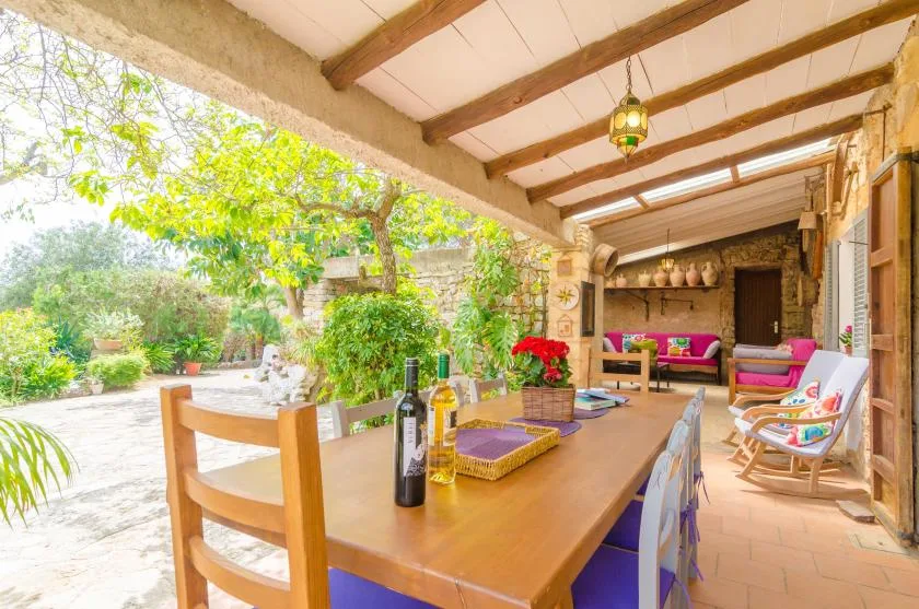 A covered patio dining area opens onto a leafy garden, with a long table and seating.