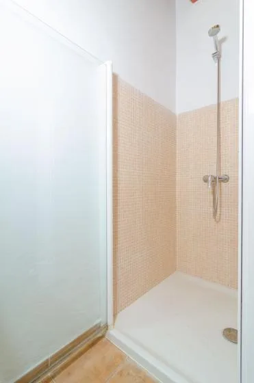 A shower with beige tiled walls and a frosted glass panel.