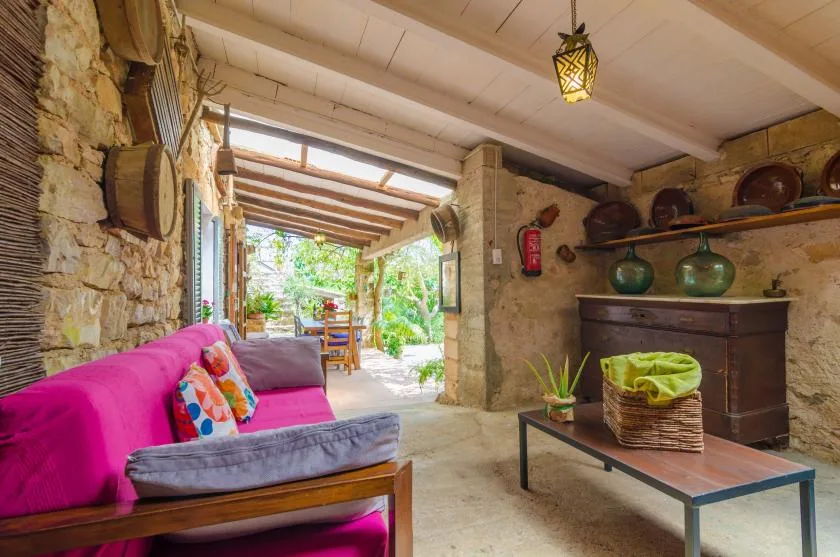 A rustic living area opens onto a covered patio, with colorful seating and a low table.