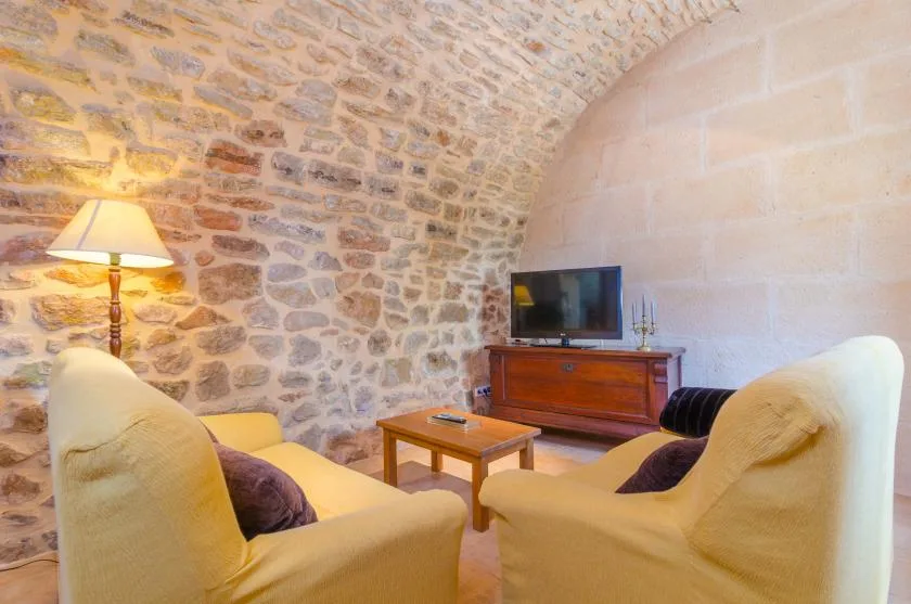 A stone-walled living room has seating, a coffee table, and a television.