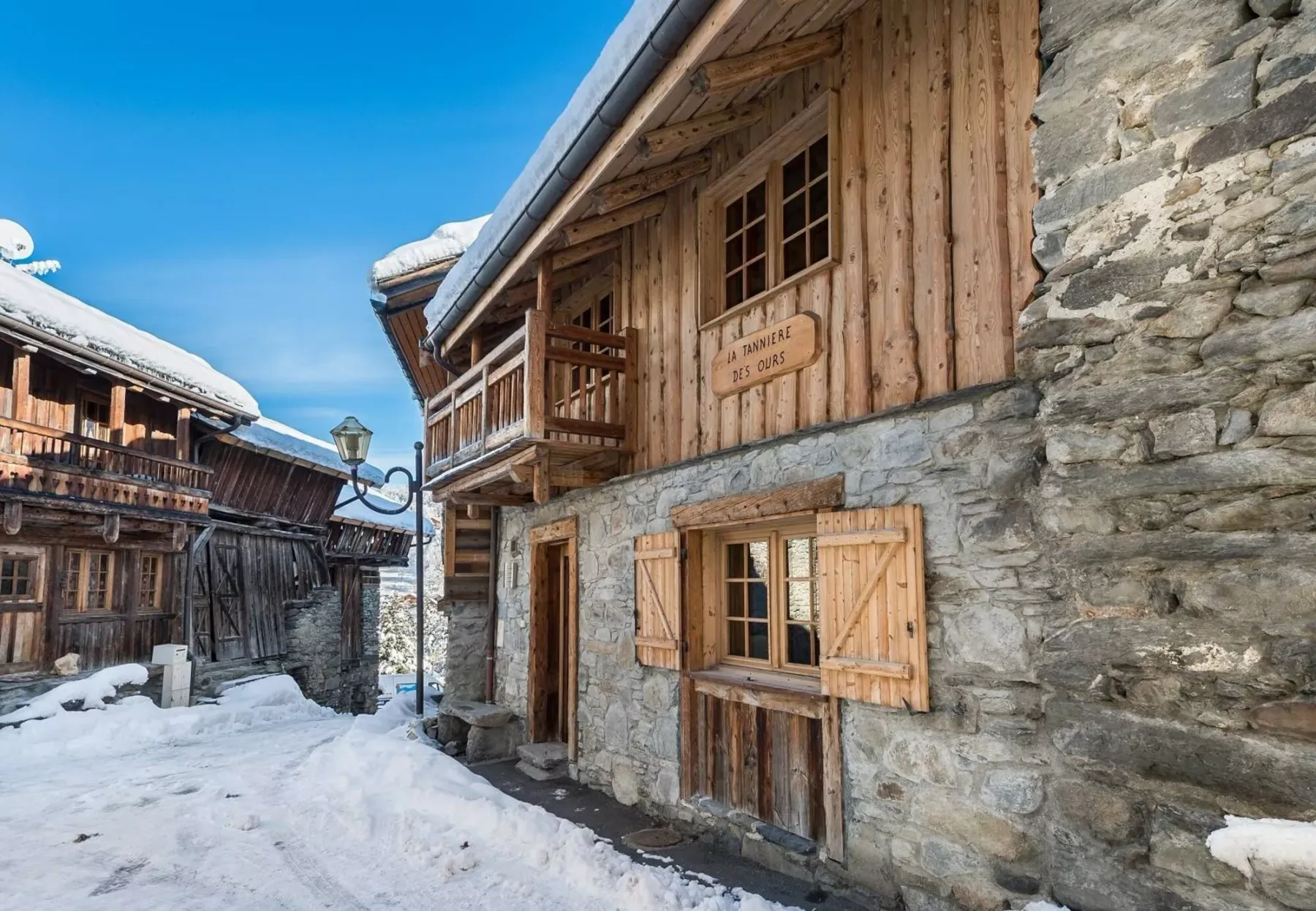 A snow-covered village lane runs between rustic stone-and-wood buildings.