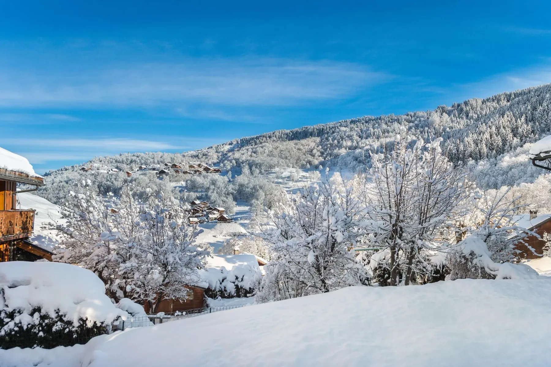 Snow-covered mountain homes and trees sit beneath a clear blue sky.
