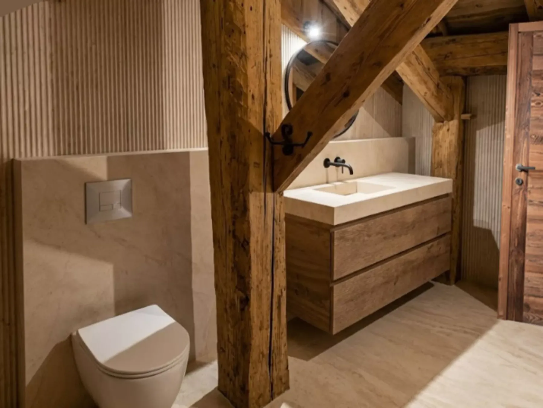 A bathroom with a wall-mounted toilet and a wood vanity beneath a mirror.