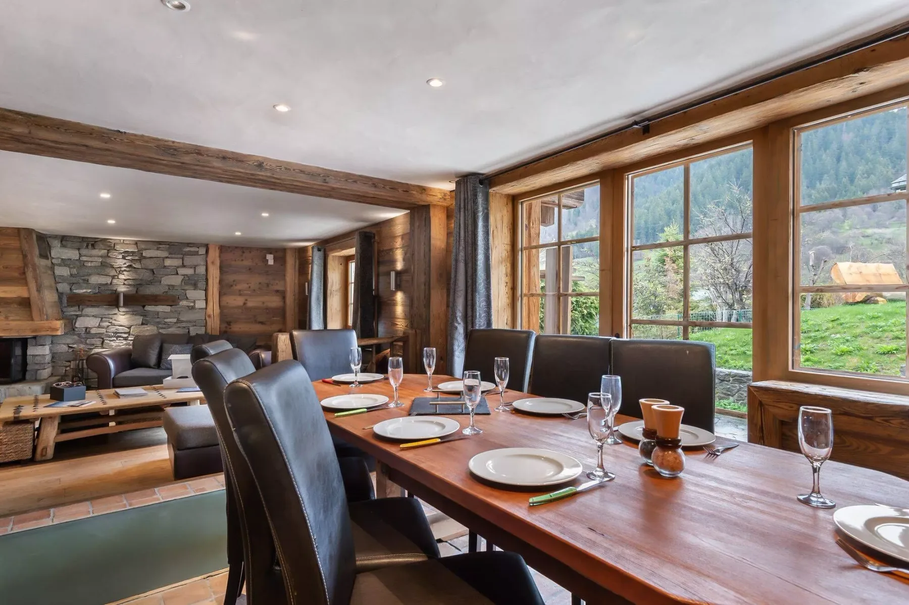 A dining area with a long wooden table and large windows overlooking a green landscape.