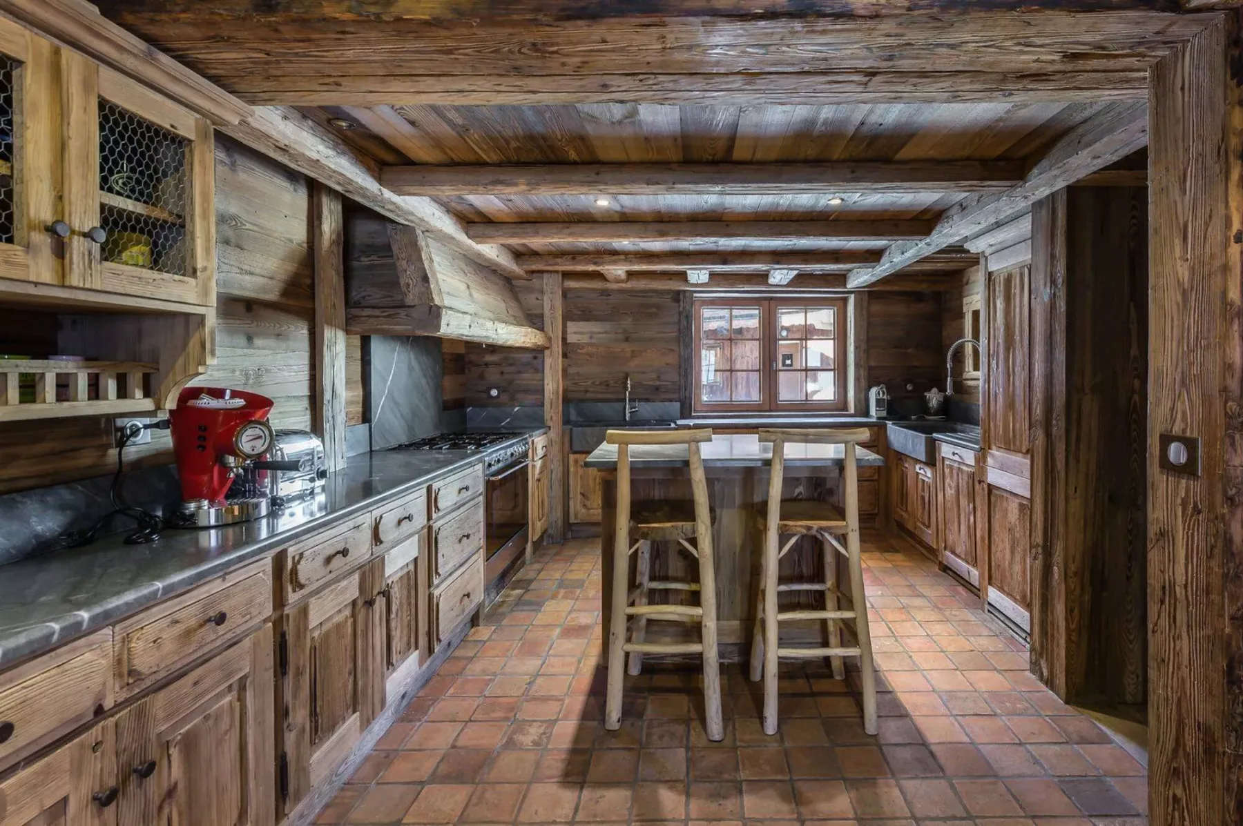 A rustic kitchen with wooden cabinets, a central island, and tiled flooring.