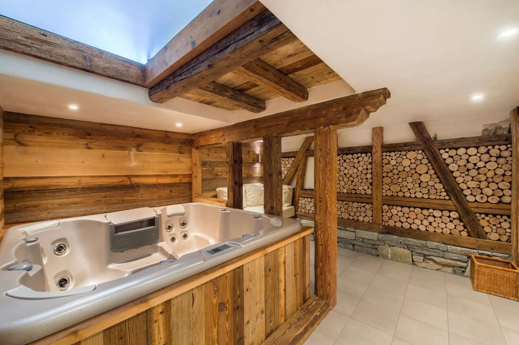 A wooden hot tub sits in a rustic room with log-stacked walls.
