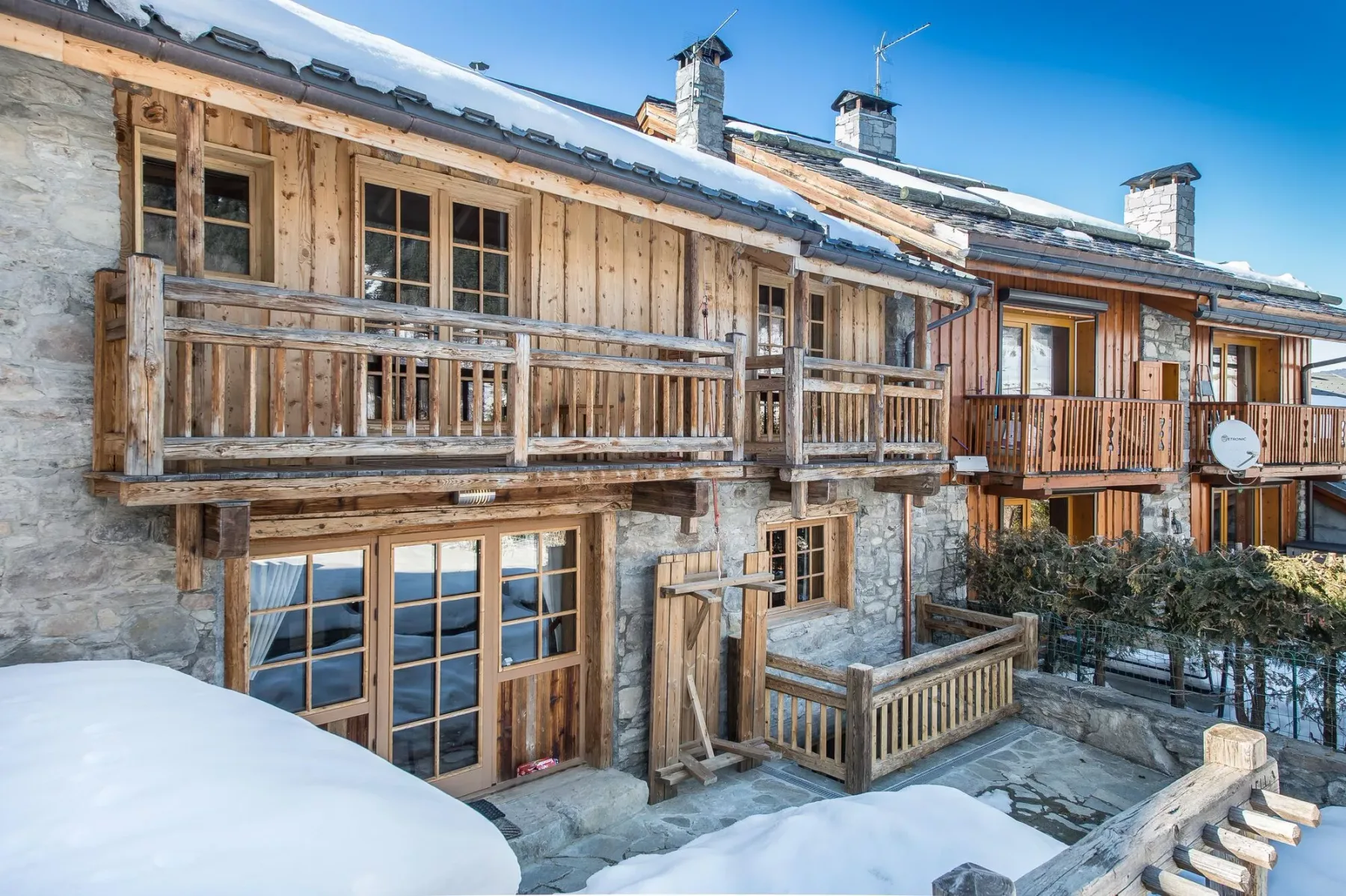 A chalet exterior with wooden balconies and snow along the ground.
