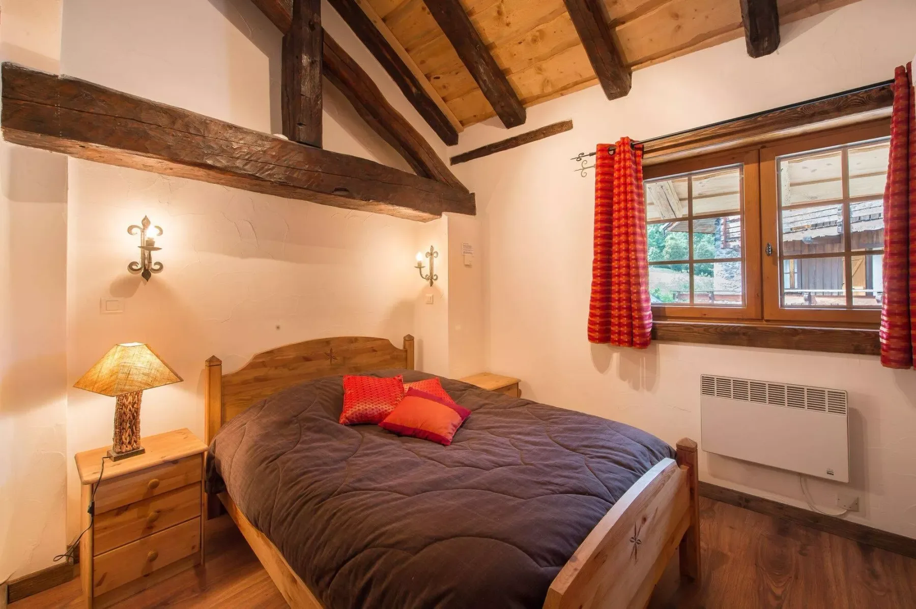A bedroom with a wooden bed beneath exposed ceiling beams and a window.