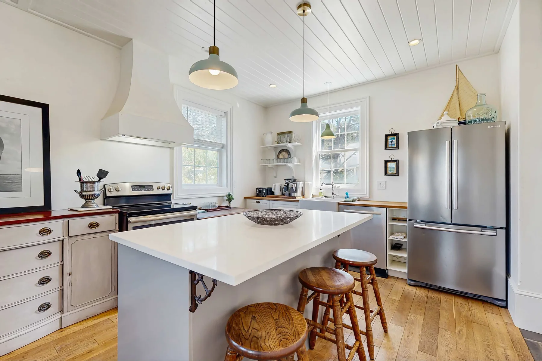 A bright kitchen with a large island, wooden stools, and stainless steel appliances.