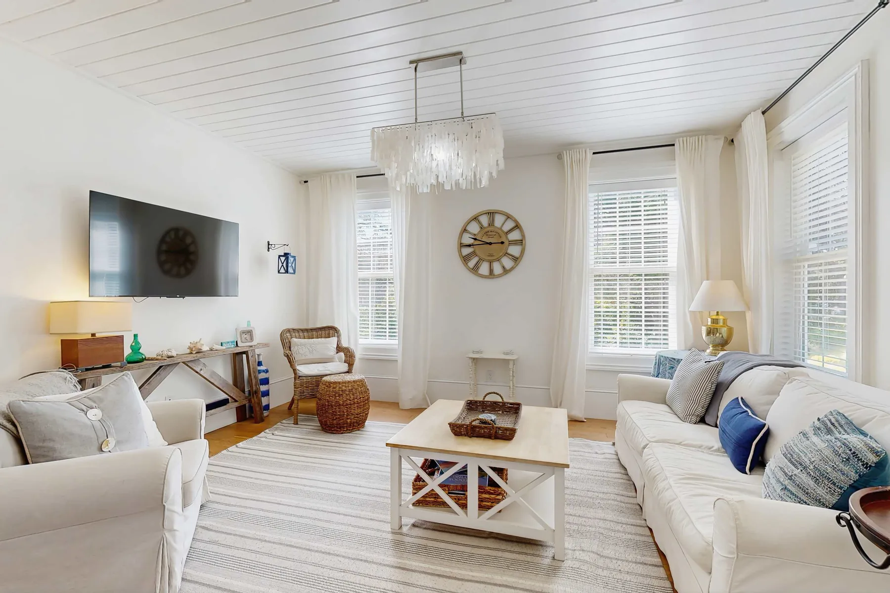 A bright living room with light seating and a coffee table beneath a chandelier.
