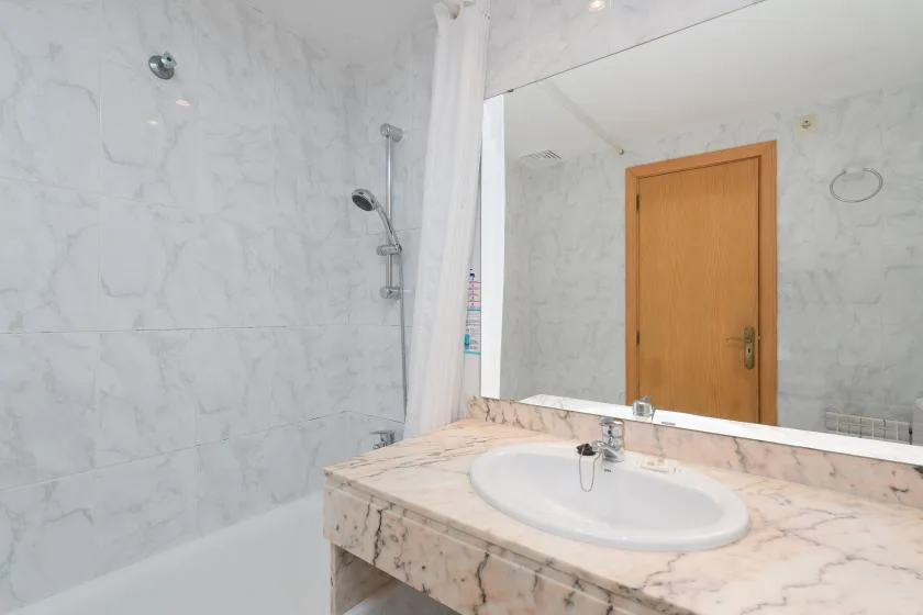A bathroom with a sink, mirror, and shower behind a curtain.