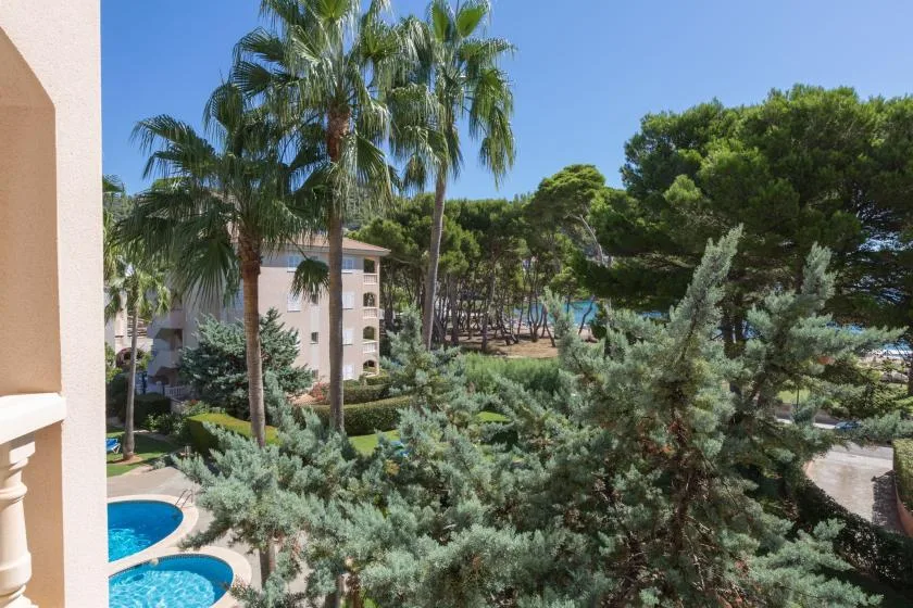 A balcony overlooks a swimming pool, palm trees, and a landscaped courtyard.