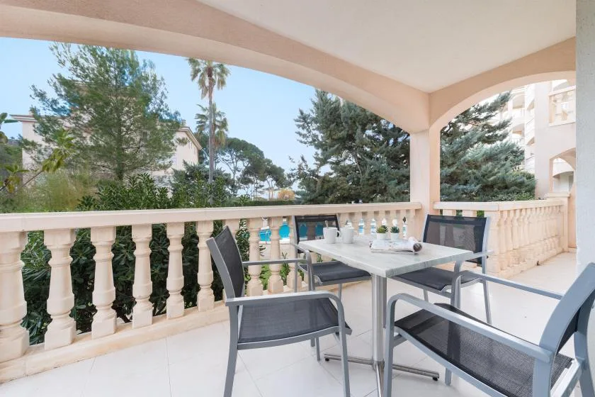 A covered outdoor dining area with a table and seating overlooks trees and nearby buildings.