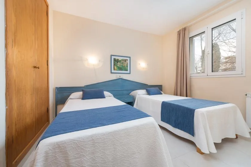 A bedroom with two beds dressed in white linens and blue runners.