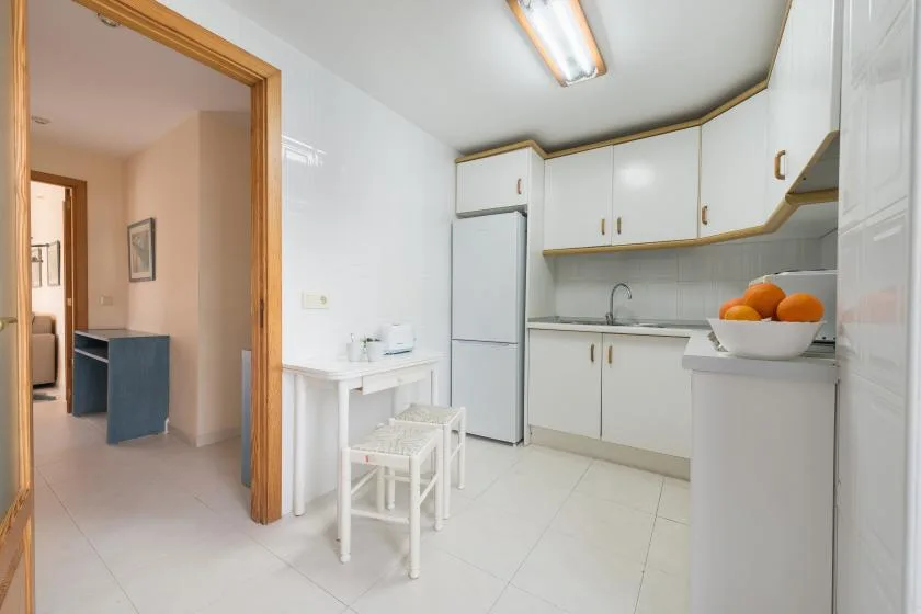 A bright kitchen with white cabinets, a refrigerator, and fruit on the counter.