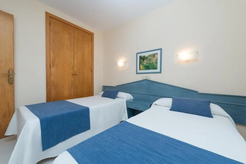A bedroom with two beds dressed in white linens and blue bedspreads.