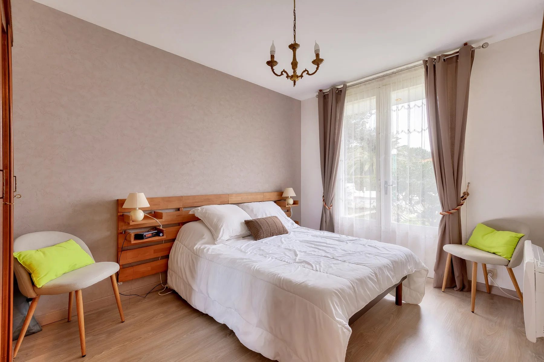 A bedroom with a double bed and a large curtained window.
