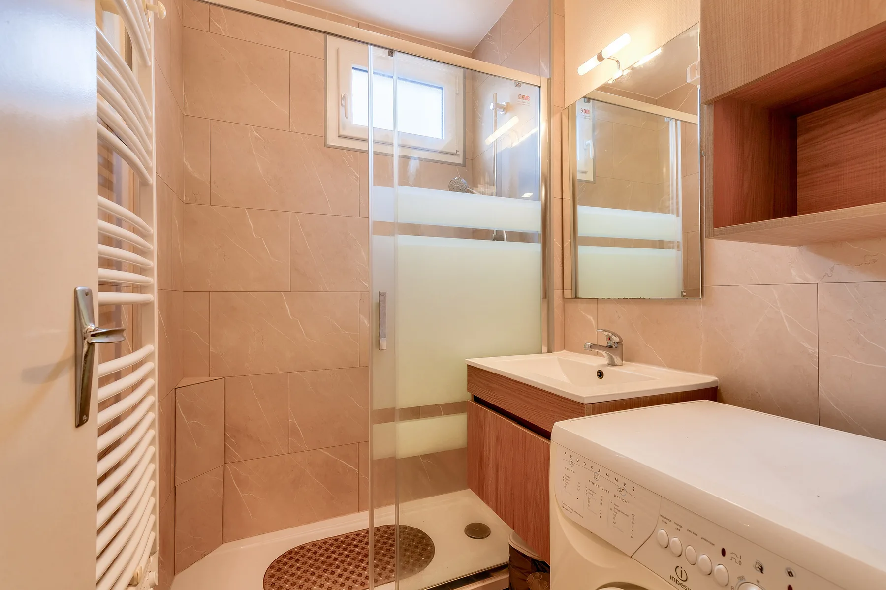 A tiled bathroom with a glass shower, sink, and washing machine.