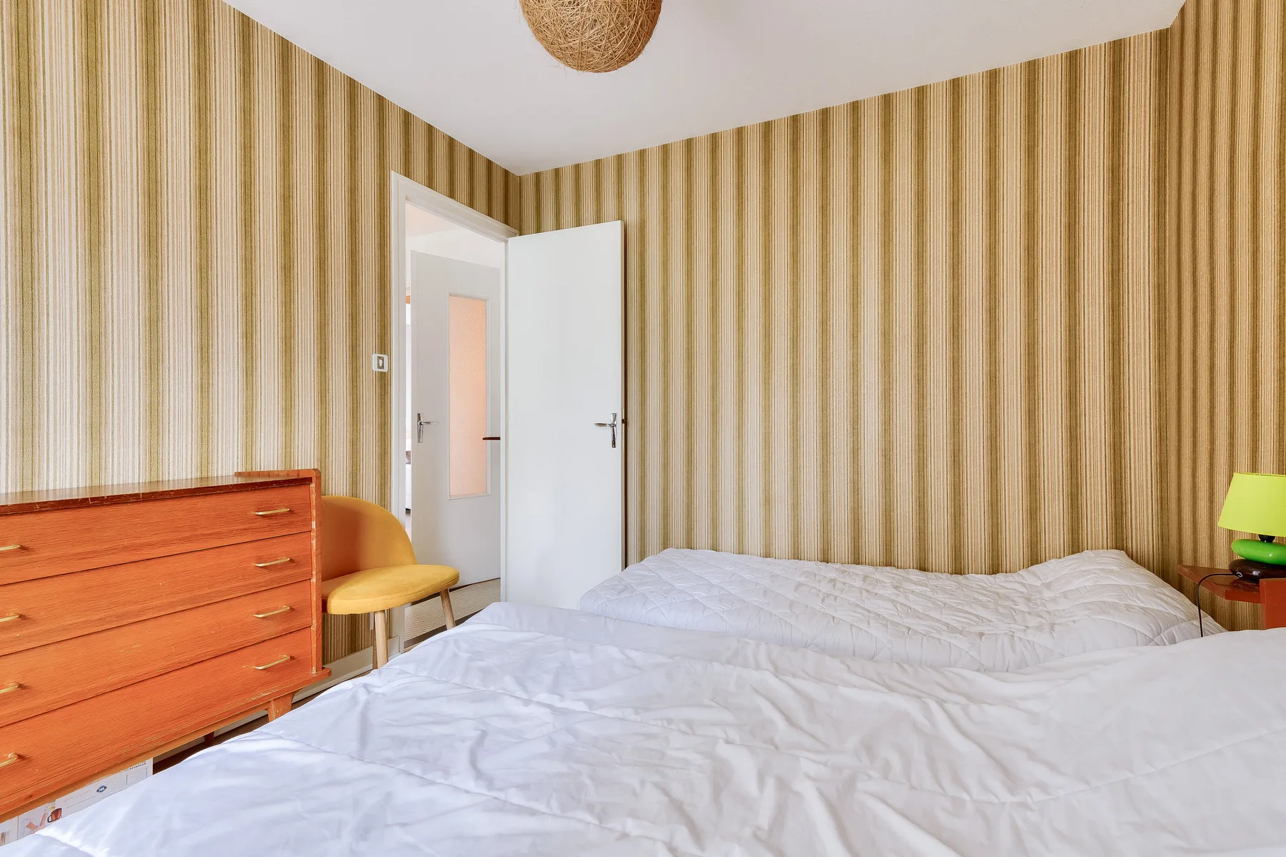 A bedroom with a bed, striped wallpaper, and a wooden dresser.