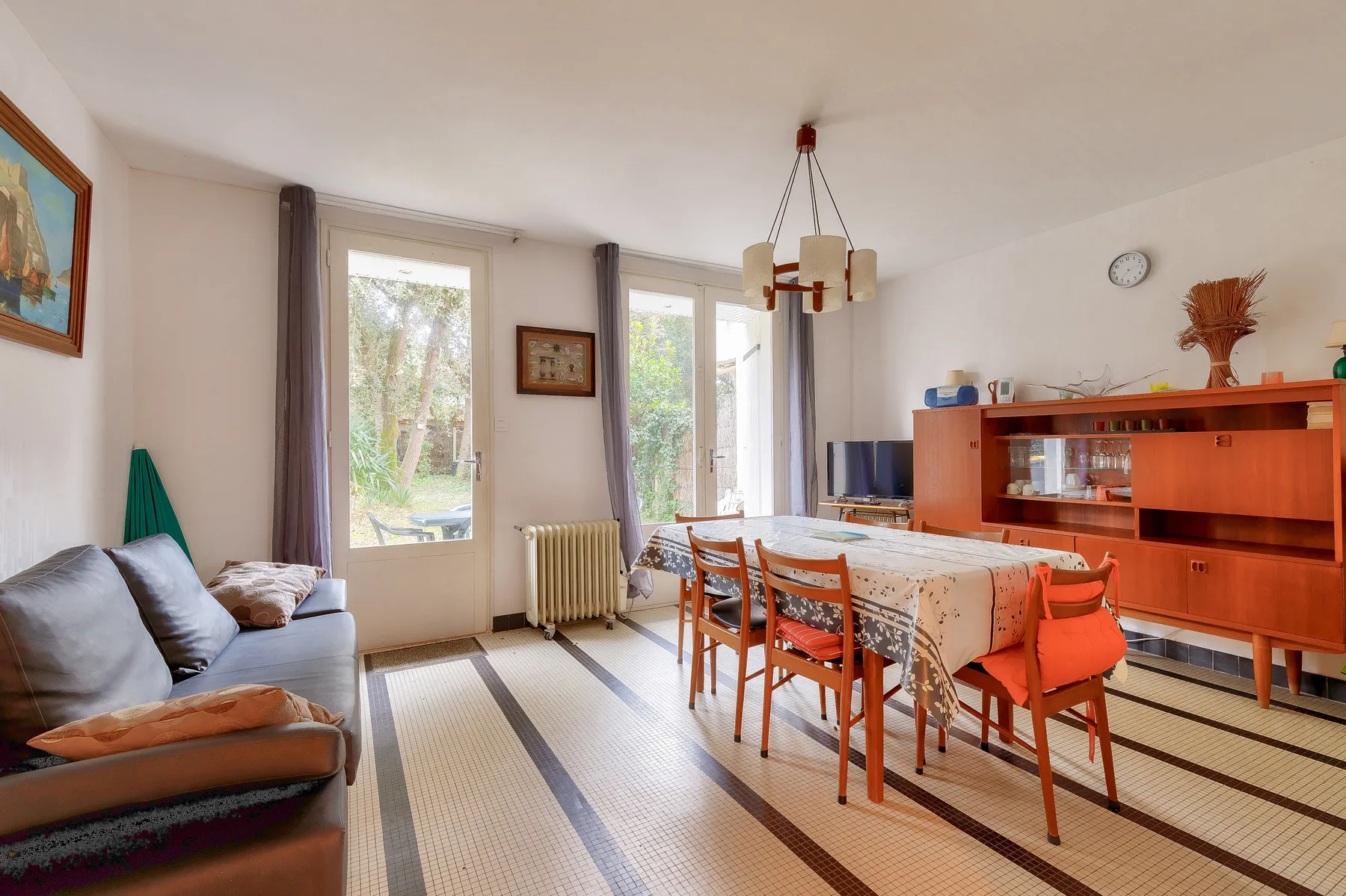 A living and dining room with a sofa, table, and chairs beside large windows.