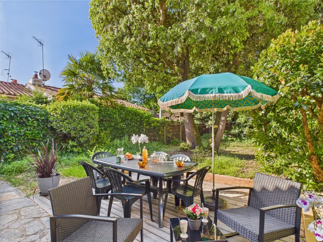 An outdoor dining area sits beneath a green umbrella in a leafy garden.