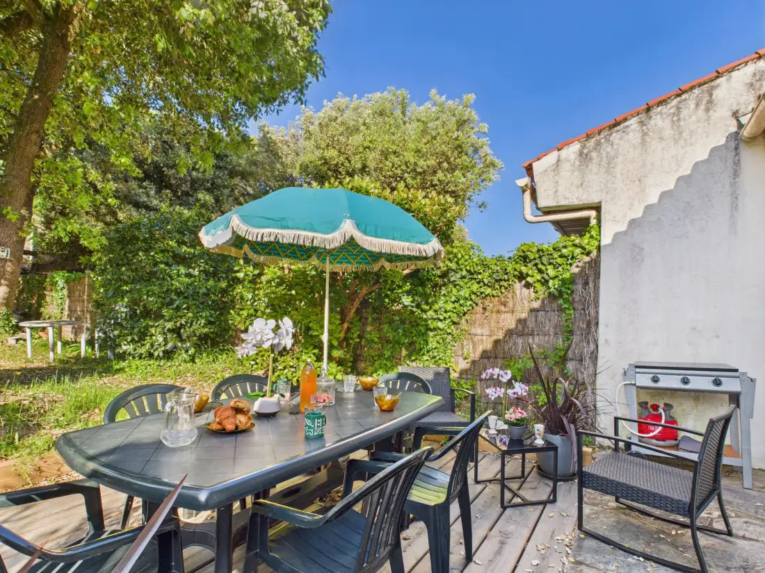 An outdoor dining area with a table and umbrella sits beside a garden.