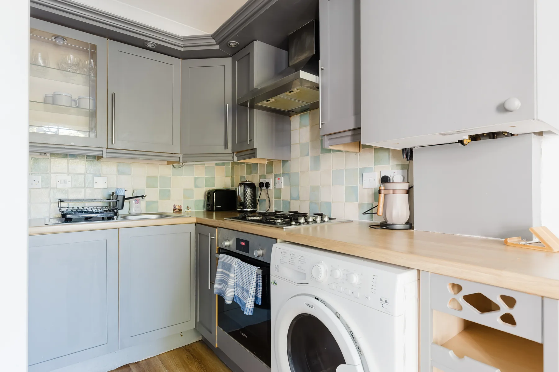 A compact kitchen with pale cabinets, a countertop, and cooking appliances.