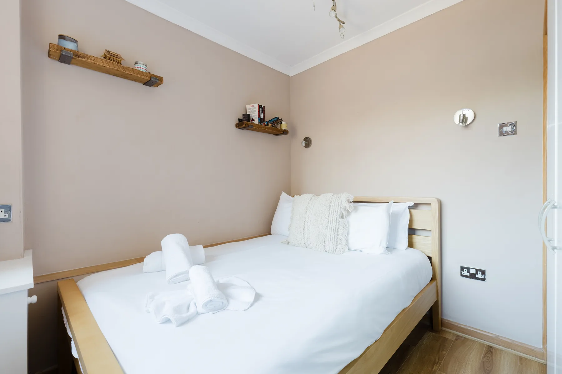A bedroom with a neatly made bed and small wall shelves.