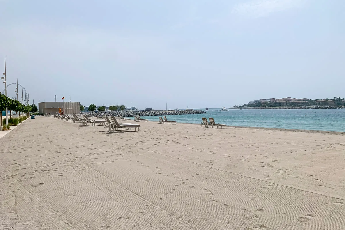 A sandy beach stretches beside calm water, with loungers along the shore.