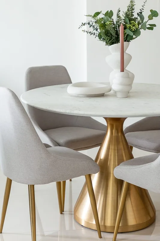 A dining area with a round table, upholstered seating, and a vase of greenery.