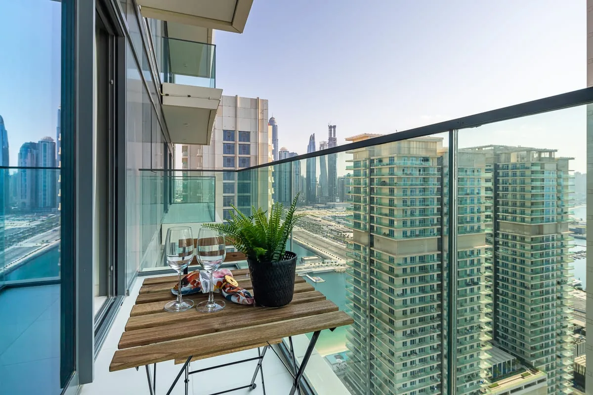 A balcony with a small table and potted plant overlooks nearby city buildings.