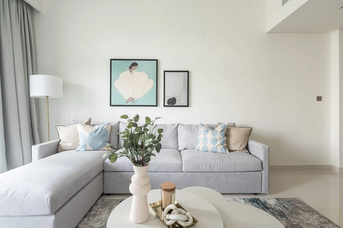Una sala luminosa con un sofá seccional gris y cuadros en la pared.