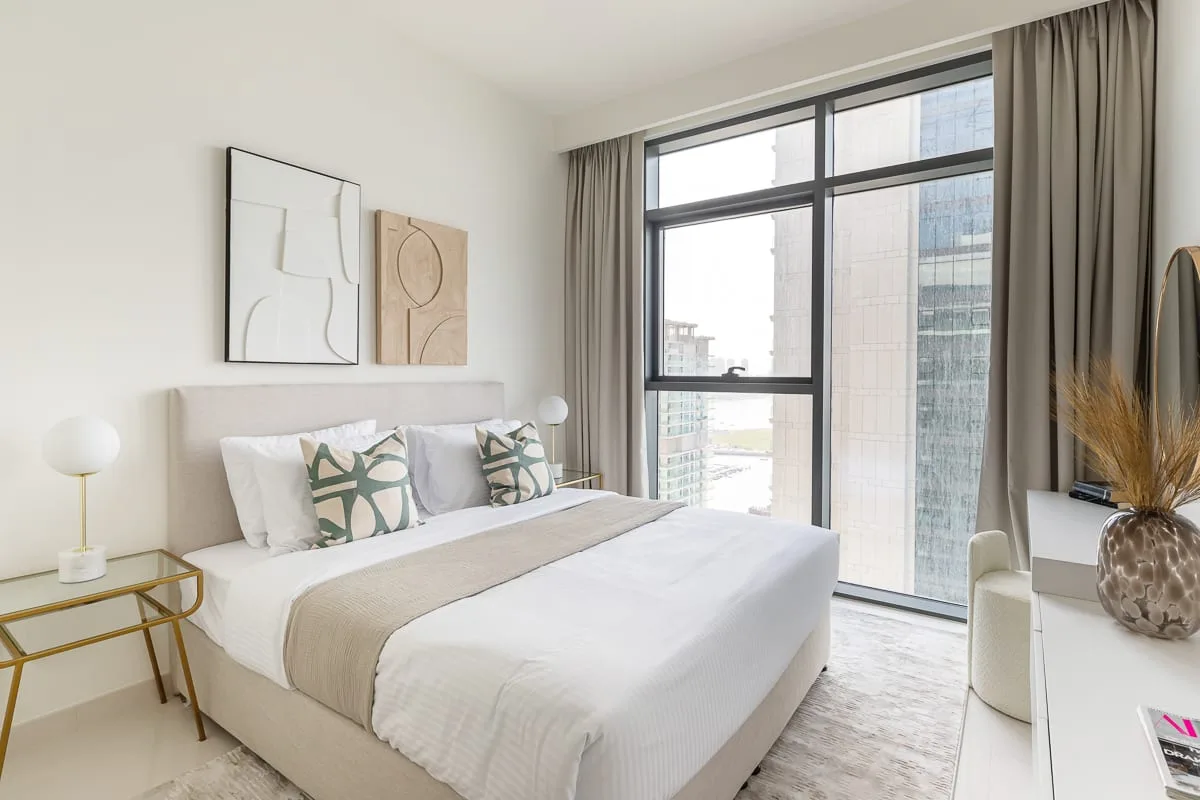 A bright bedroom with a neatly made bed beside a large window.