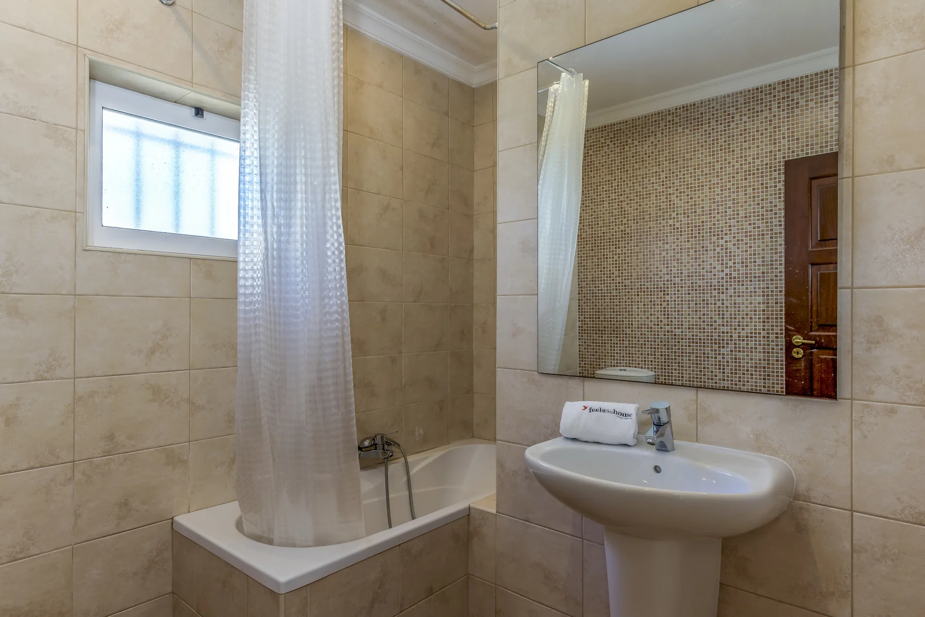 Baño alicatado con bañera, cortina de ducha y lavabo.