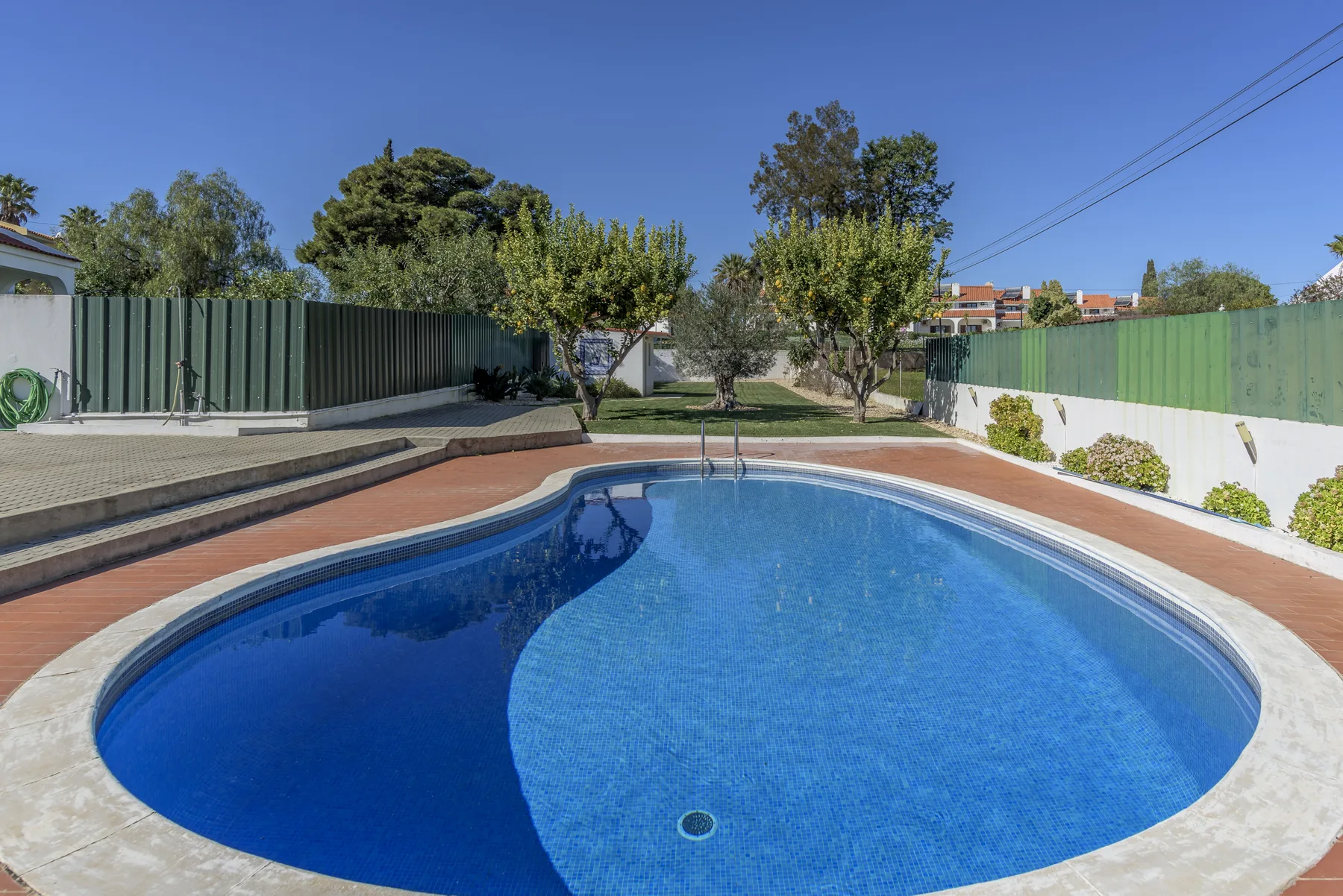 Una piscina al aire libre está rodeada por una zona pavimentada y un jardín.