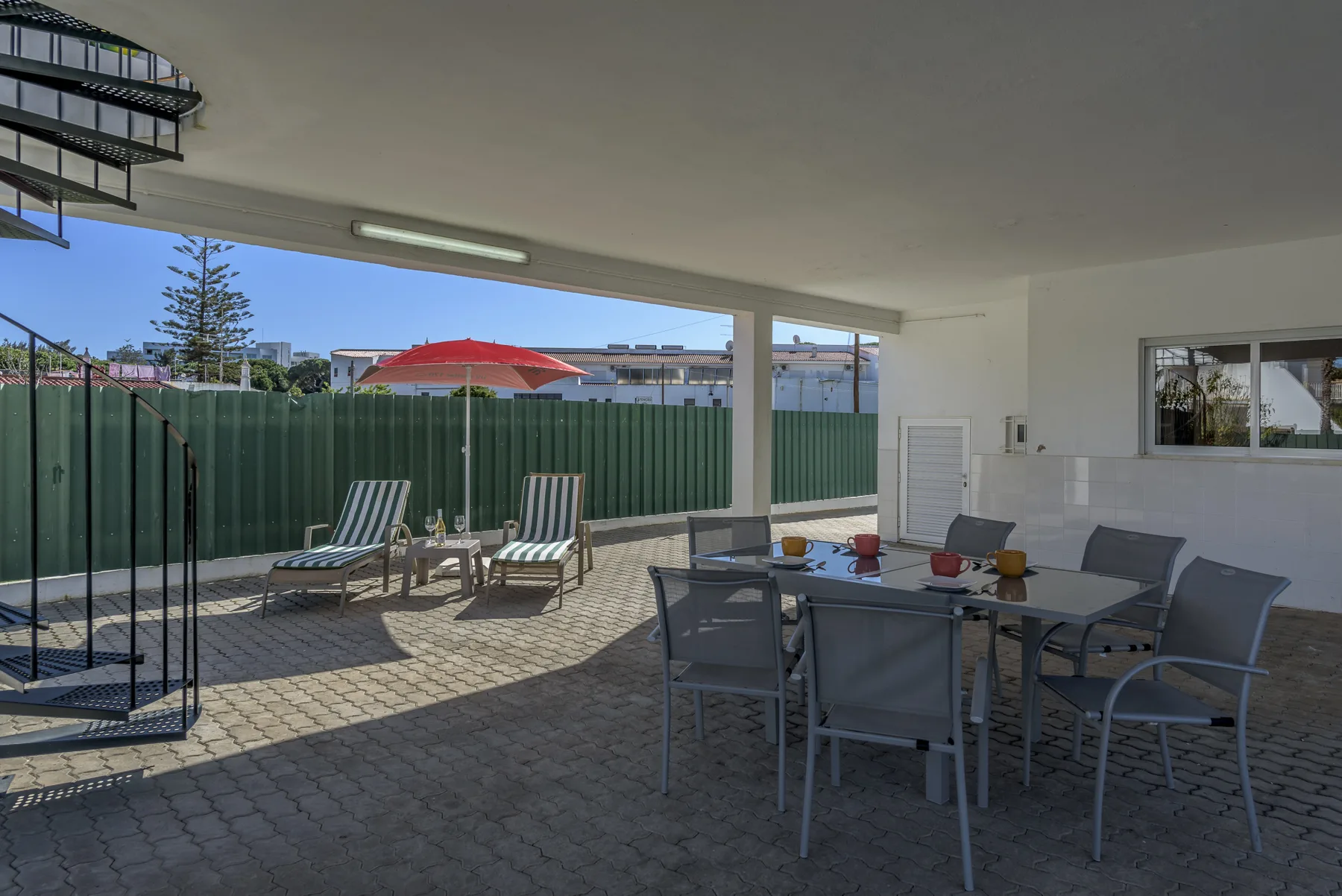Un patio cubierto tiene una mesa con sillas junto a una zona pavimentada con piscina.