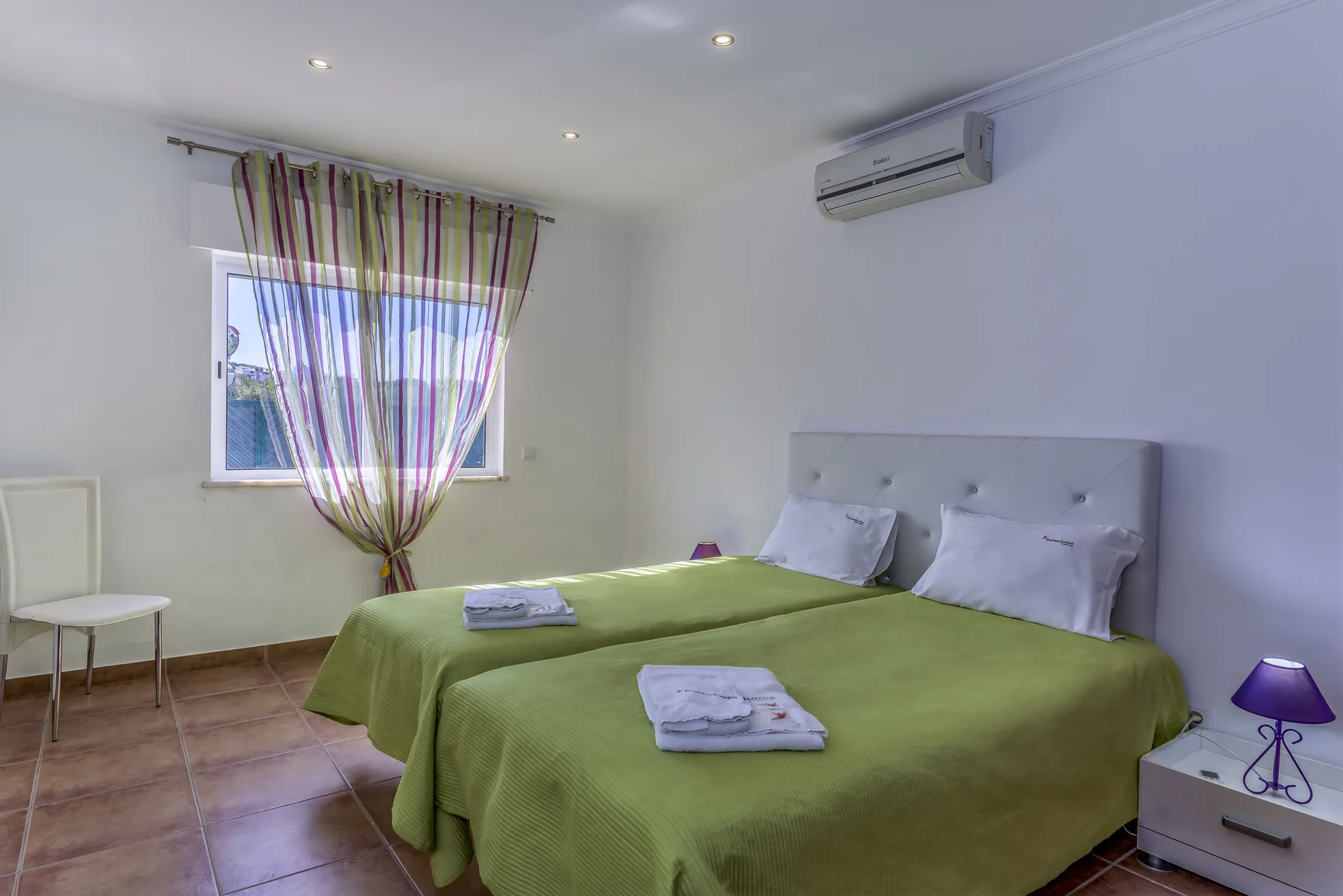 Un dormitorio con dos camas, colchas verdes y una ventana con cortinas.