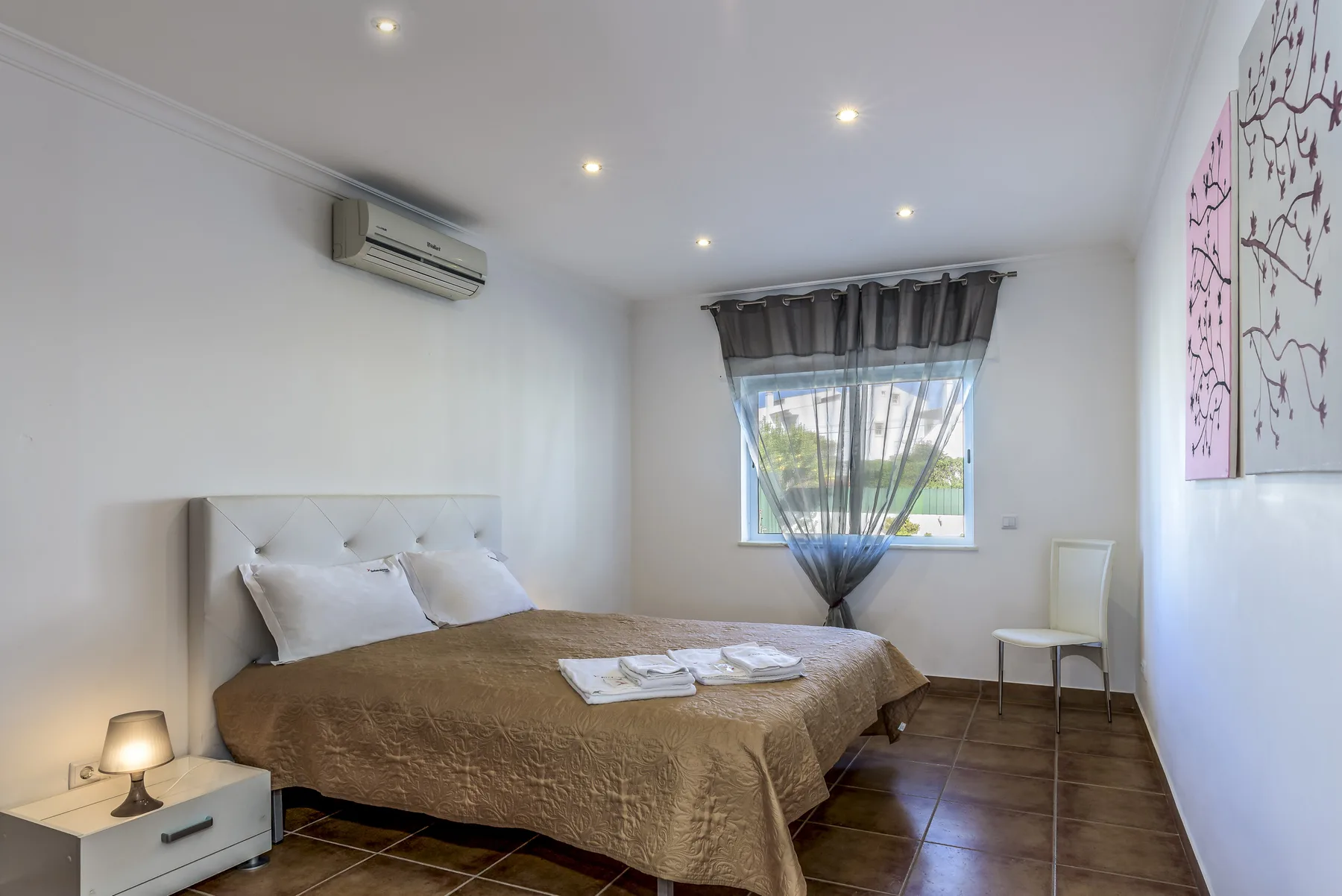 Dormitorio con una cama grande, una ventana y una pequeña mesita de noche.