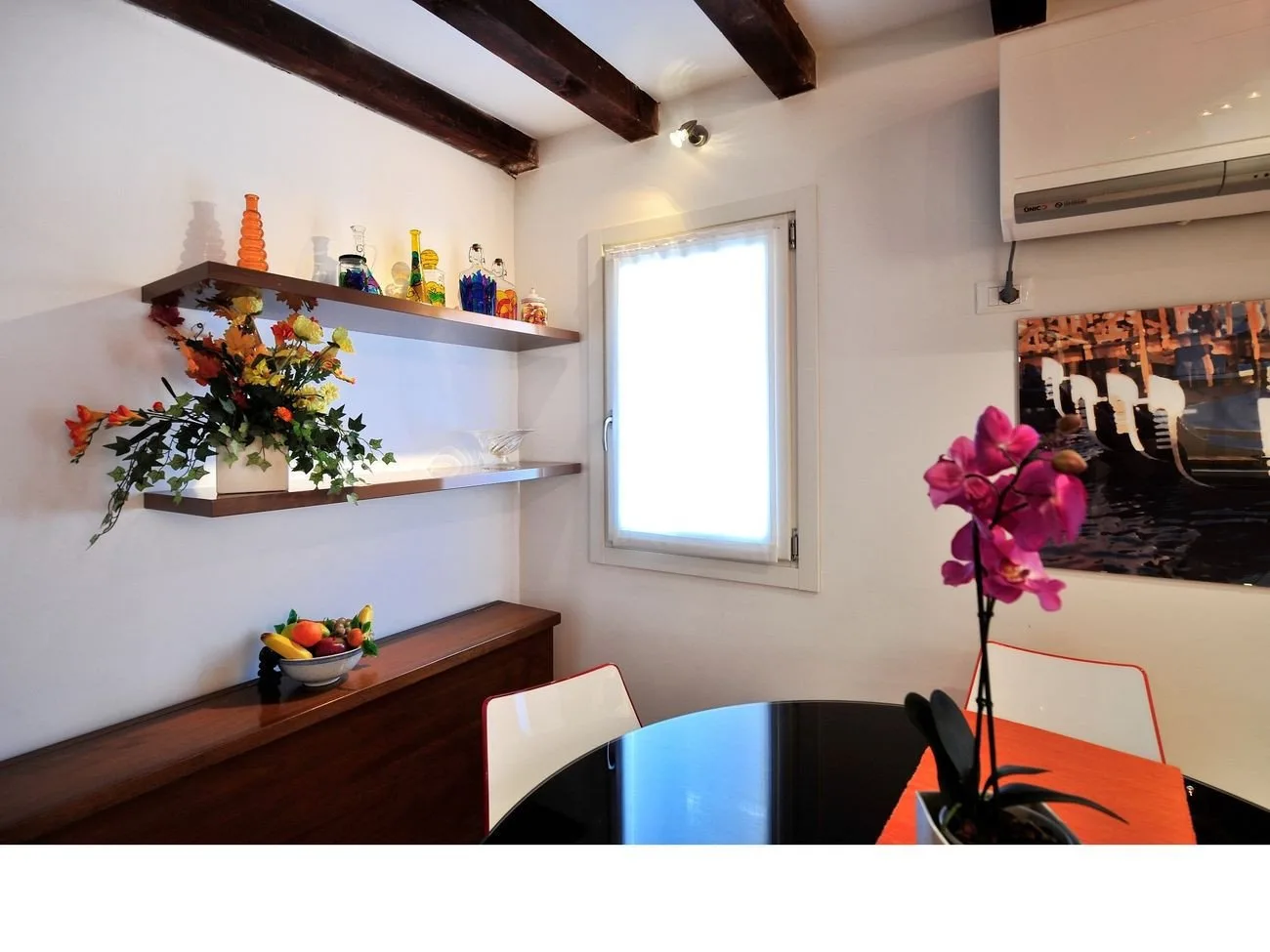 Un comedor luminoso con una mesa redonda, sillas coloridas y estantes en la pared.