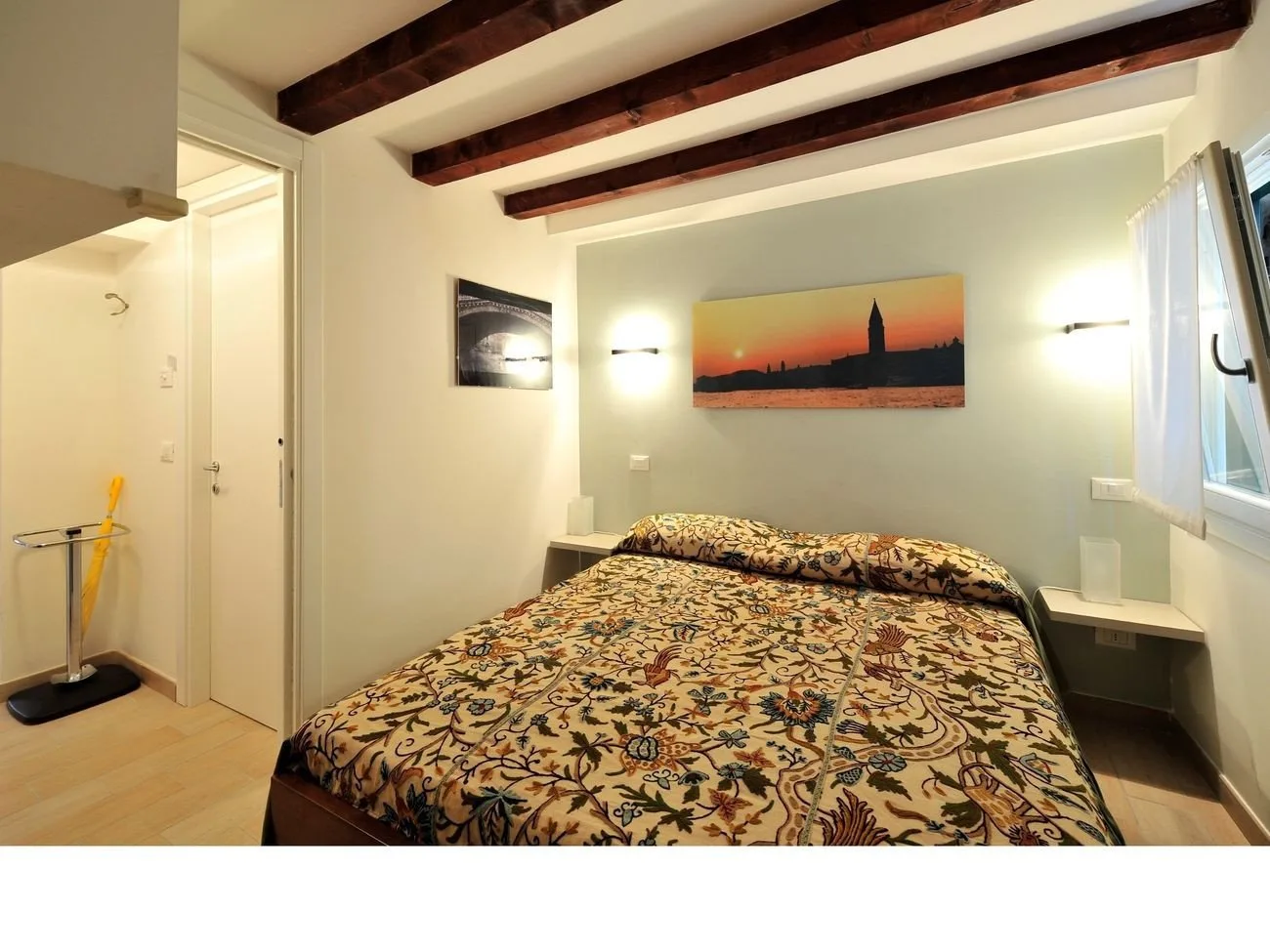 Un dormitorio con una colcha estampada, cuadros y vigas de techo a la vista.