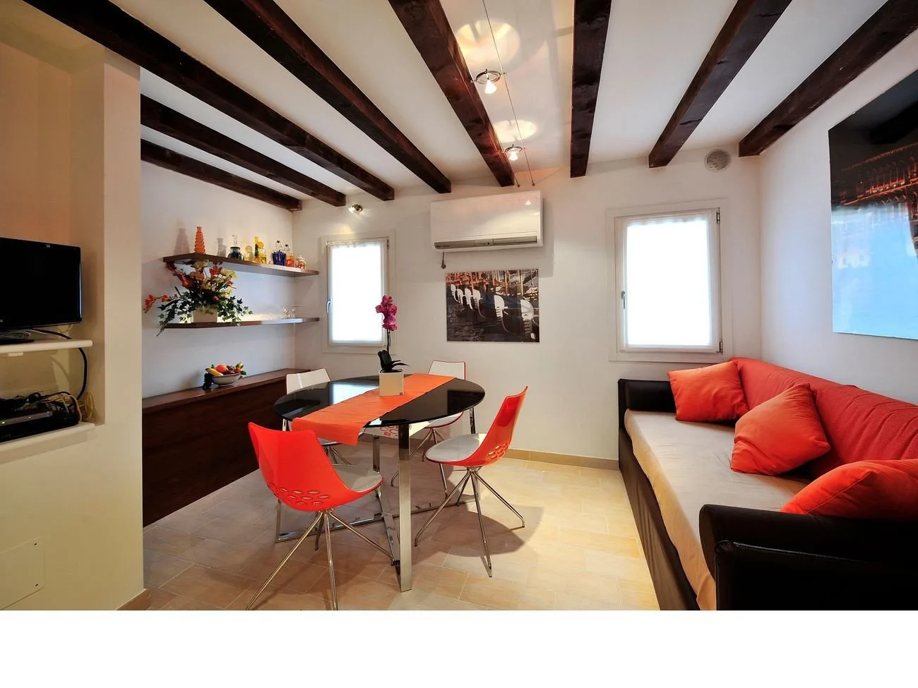Un comedor con mesa y sillas está junto a una zona de estar con cojines rojos.
