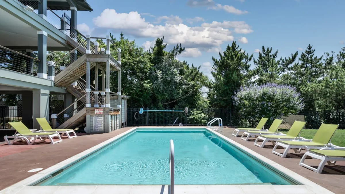 Una piscina al aire libre está rodeada de asientos reclinables y árboles.