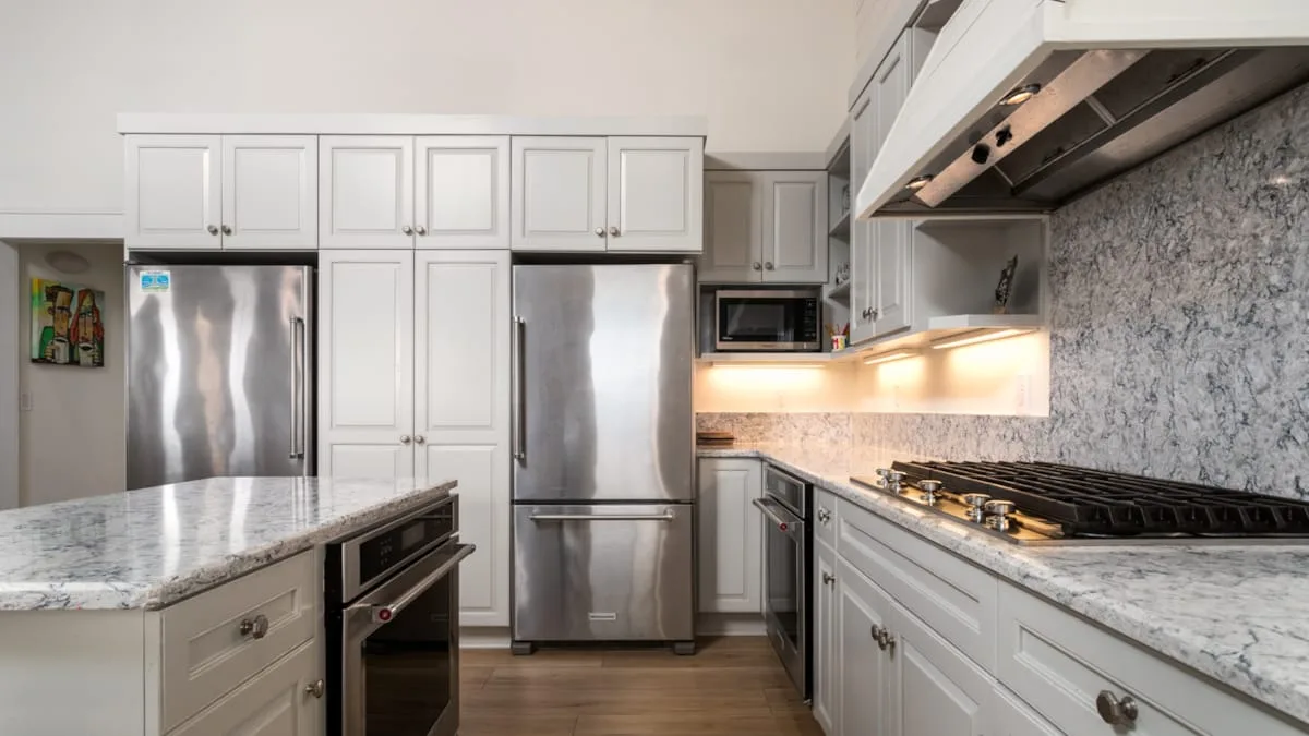 Una cocina luminosa con gabinetes blancos, electrodomésticos de acero inoxidable y encimeras de piedra.