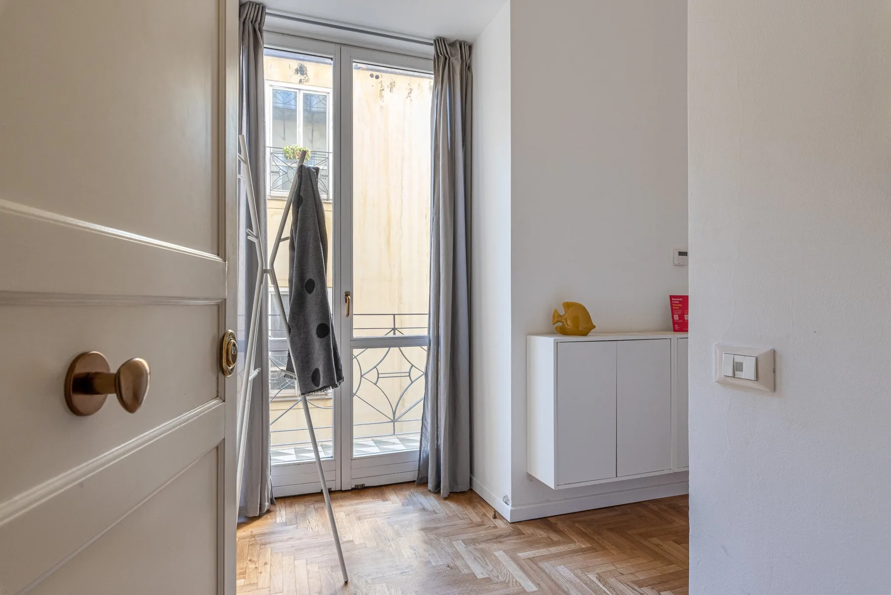 A bright room with a glass balcony door, curtains, and a light wood floor.