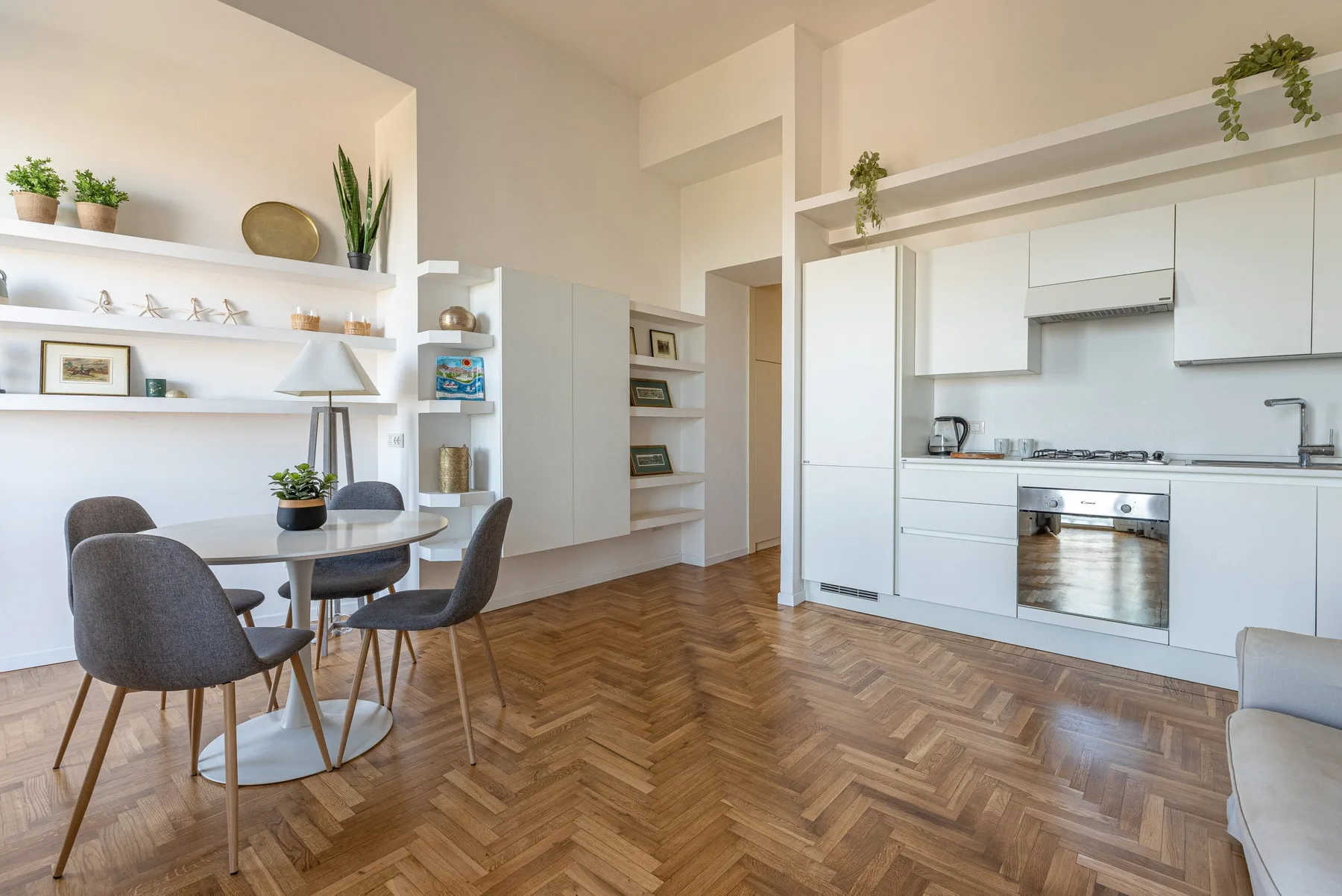 Una luminosa zona de comedor y cocina con una mesa redonda y armarios blancos.